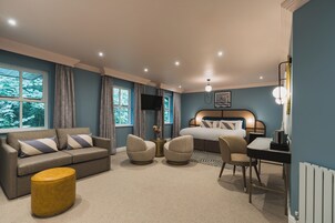Una habitación de hotel moderna con sofá, sillones, mesa de comedor, cama y televisor.