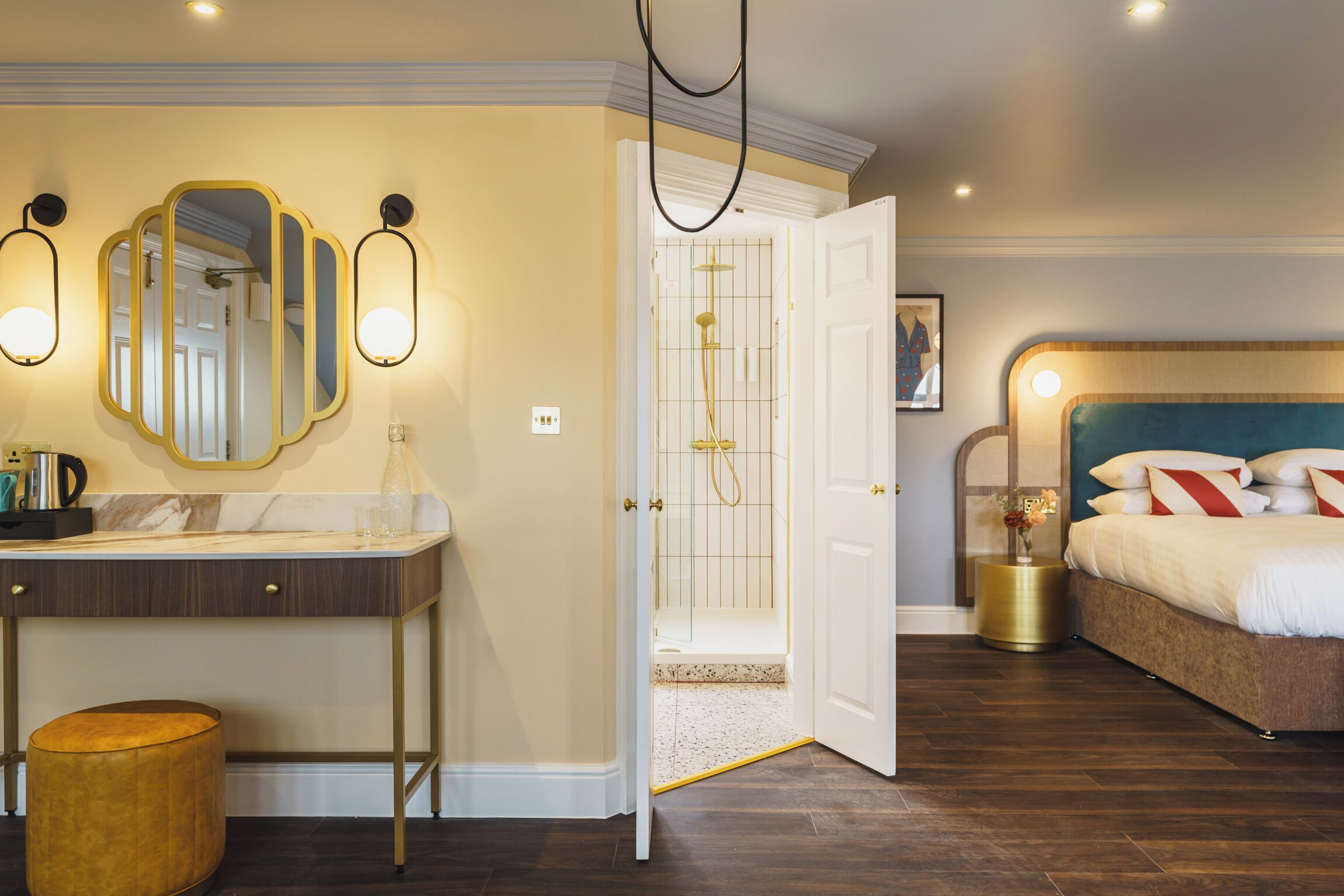 A hotel room with a bathroom, a vanity with a mirror, a bed, and a nightstand with a vase.