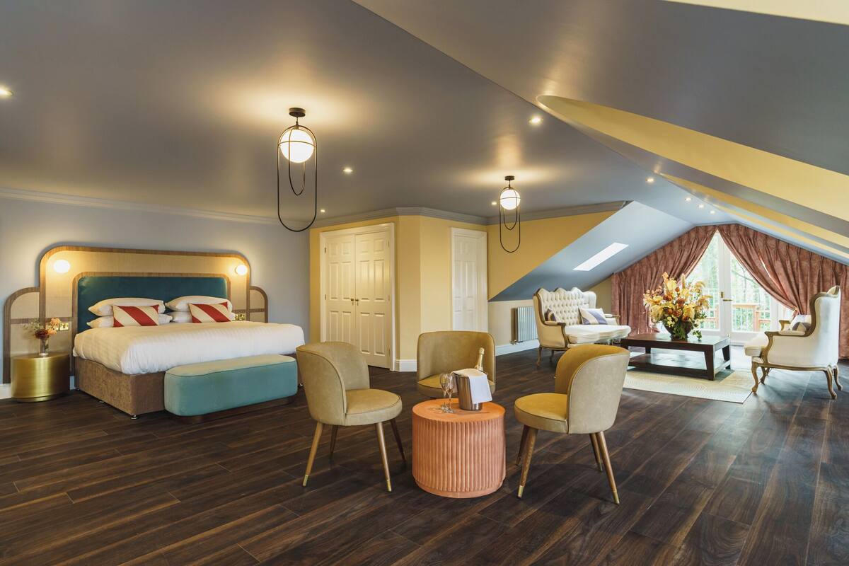 Um quarto espaçoso com uma cama grande, duas poltronas, uma mesa de centro e um espaço de estar com um sofá e cortinas.