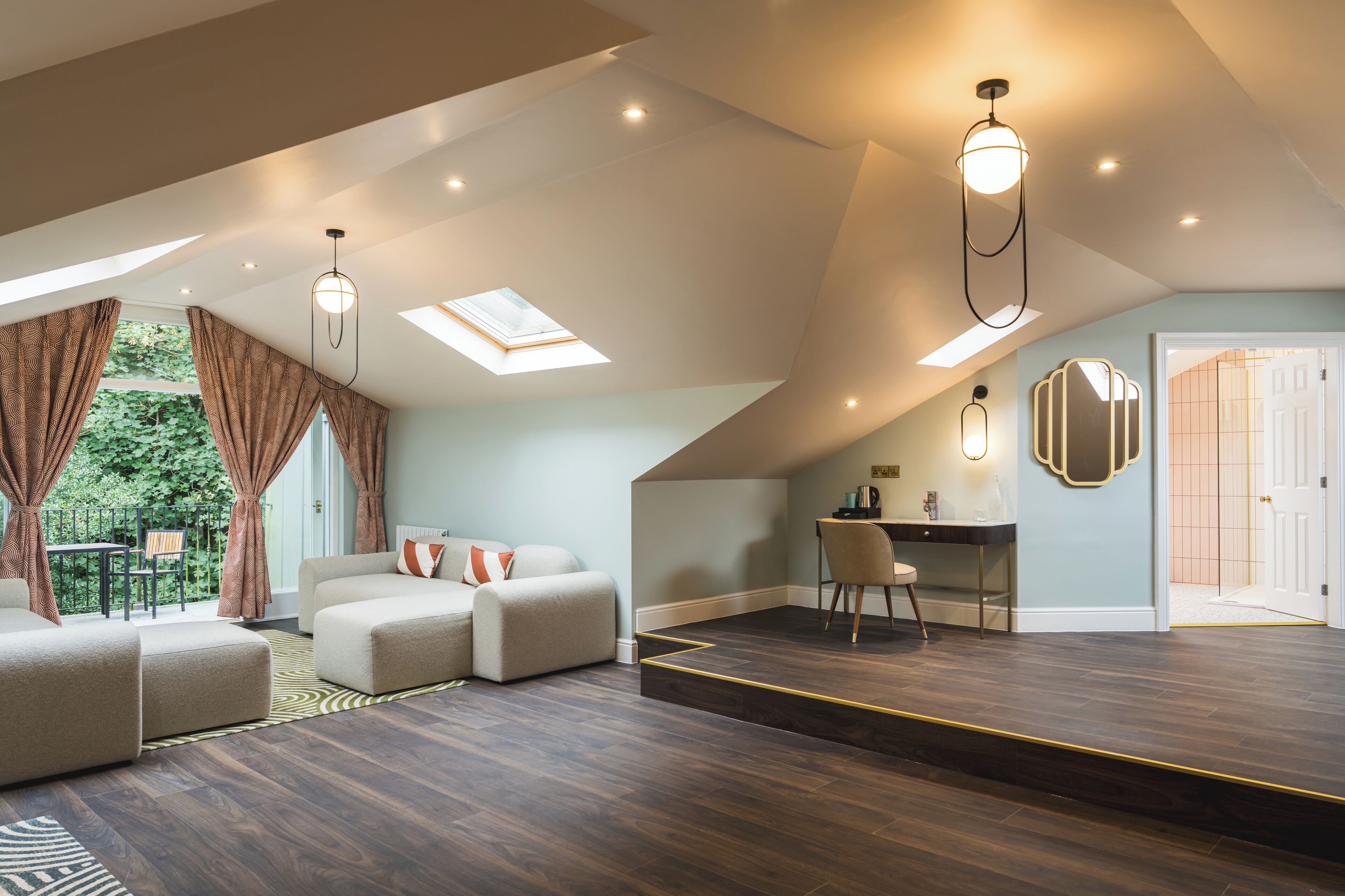 A spacious loft with a high ceiling, skylights, and a cozy seating area with a desk and chair.