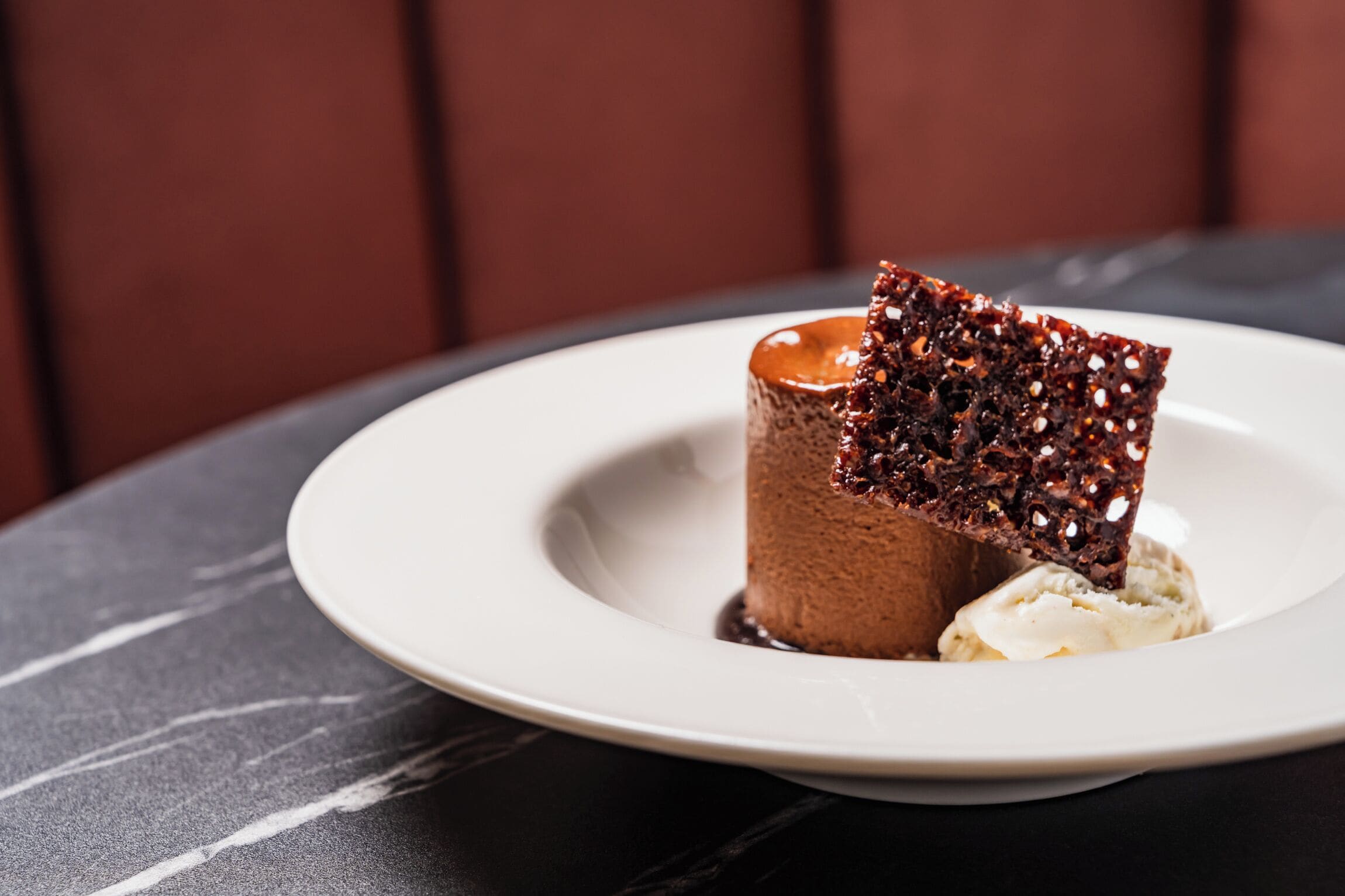 Ein Dessert auf einem weißen Teller vor einem dunkel marmorierten Tisch.
