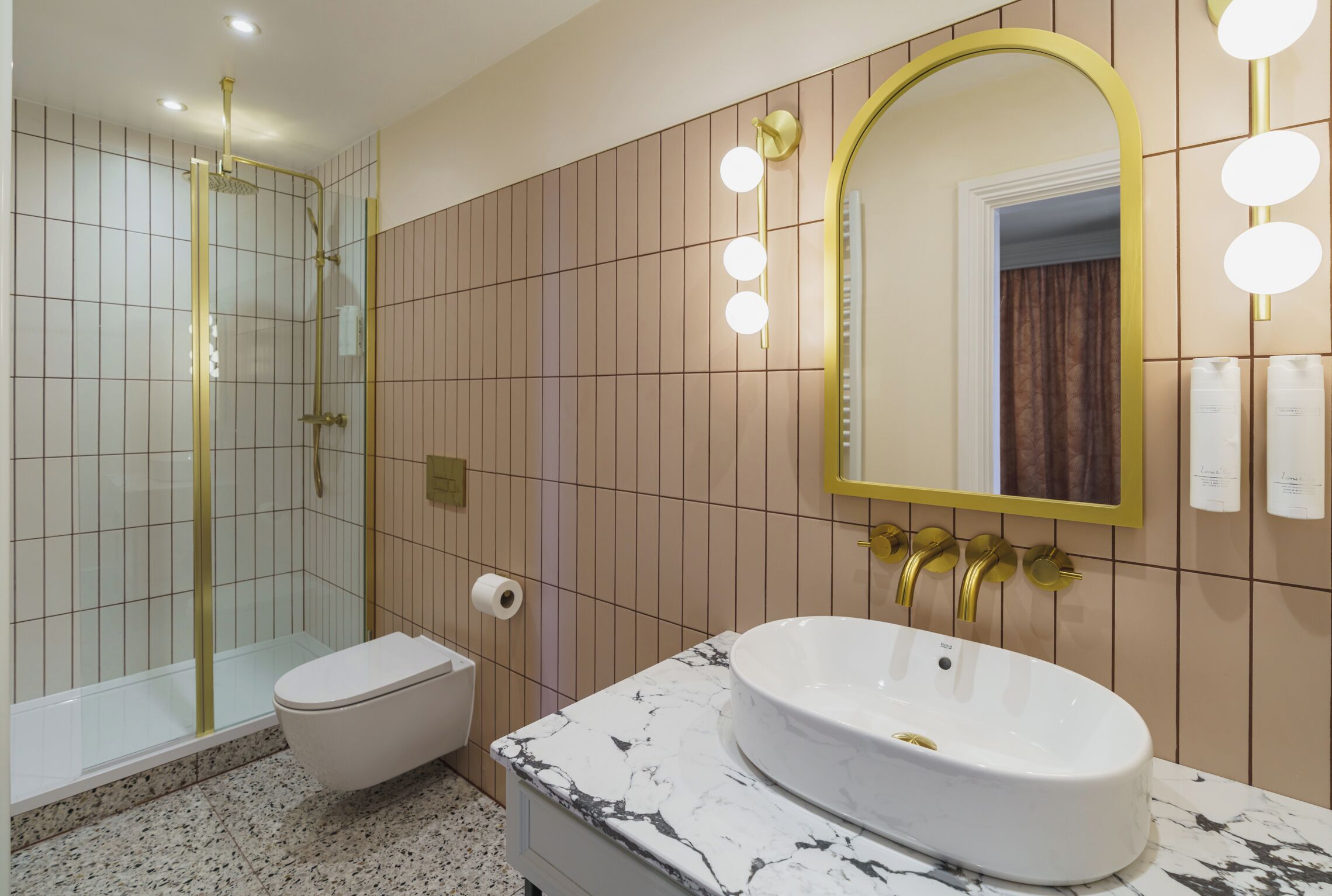 A bathroom with a glass-enclosed shower, a white toilet, a marble sink, and a mirror with lights.