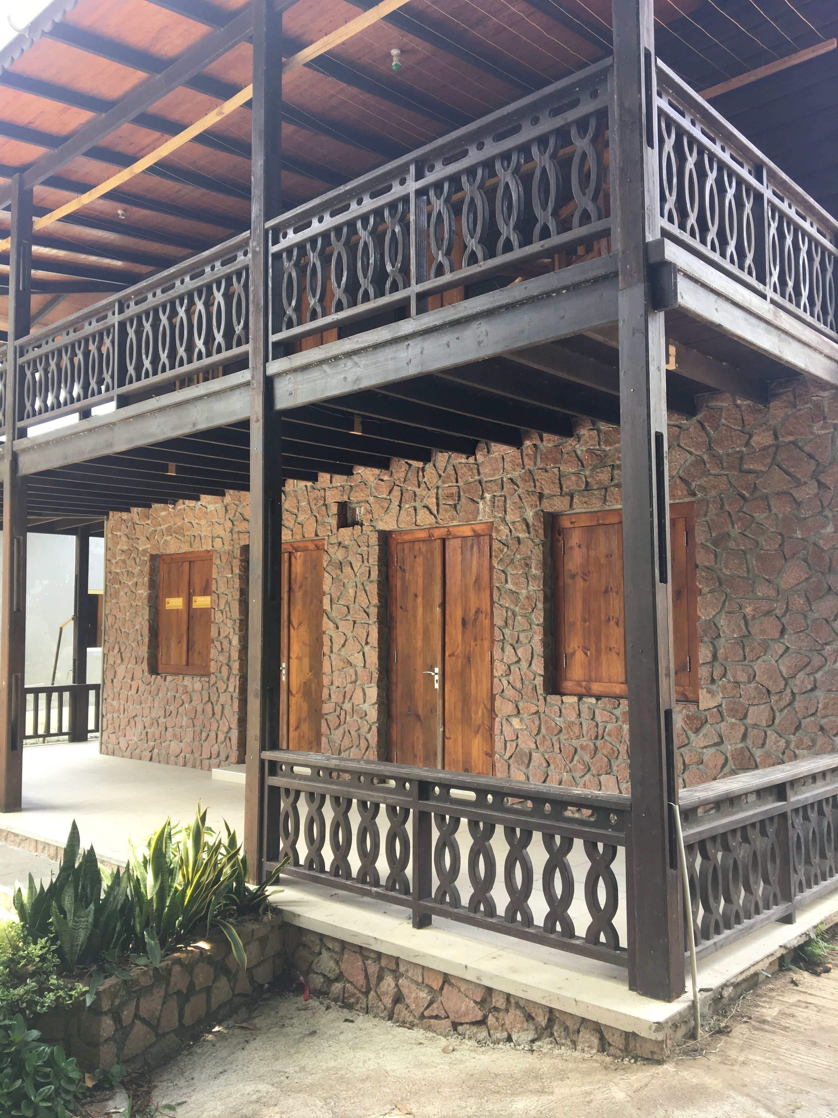 A two-story building with a stone facade, wooden doors, and a balcony with a decorative metal railing.