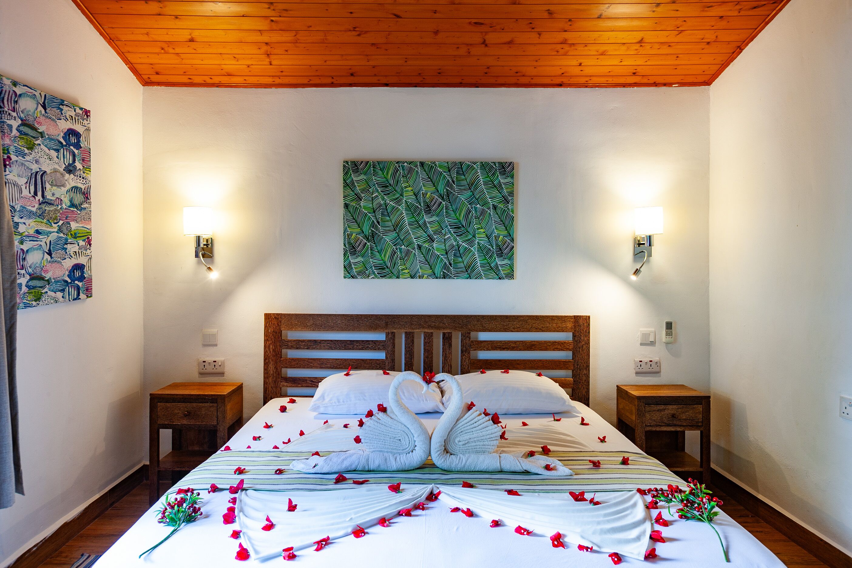 A bedroom with a wooden headboard, two bedside tables, a bed with a floral bedspread and a swan decoration, and a green abstract painting on the wall.