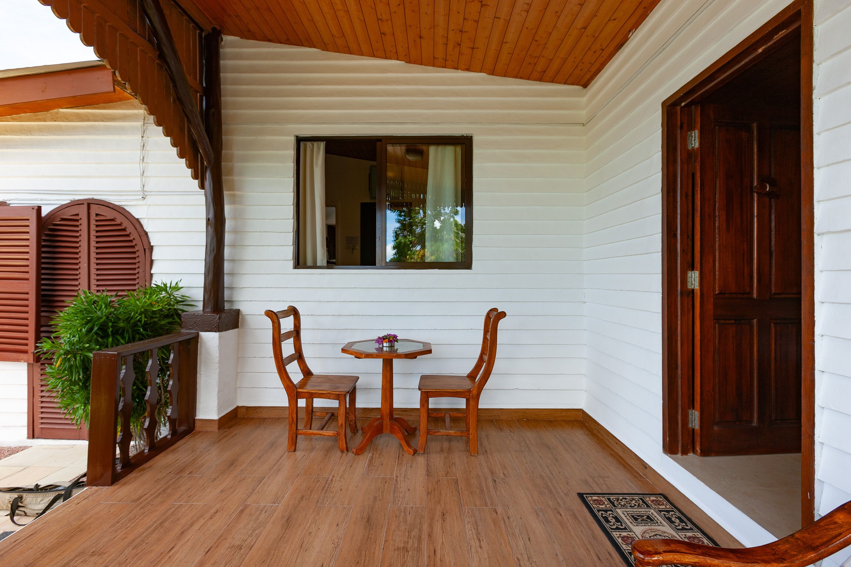 A wooden porch with a table and chairs, a window, and a door.