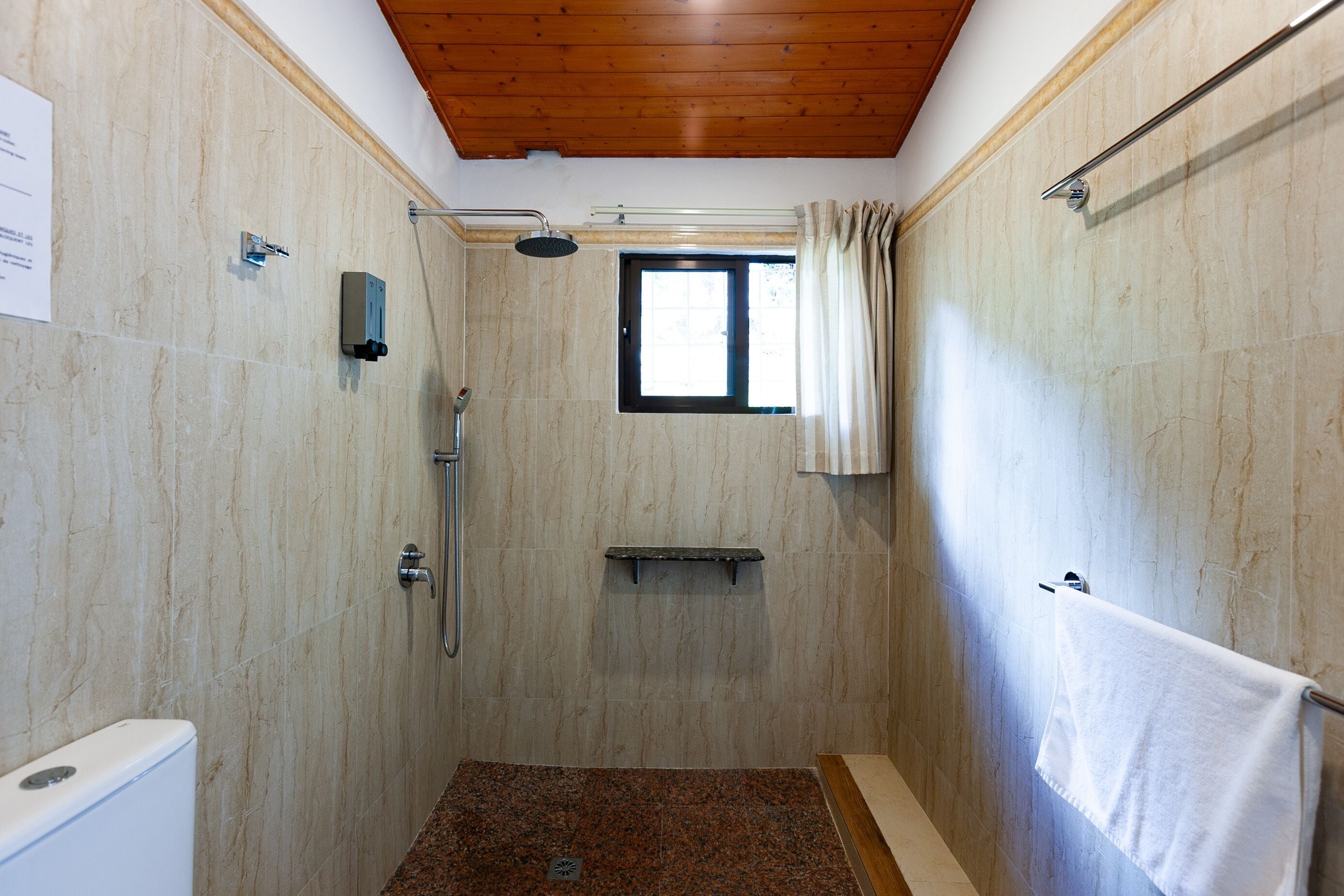 Un área de ducha con ventana, un perchero y un cabezal de ducha.