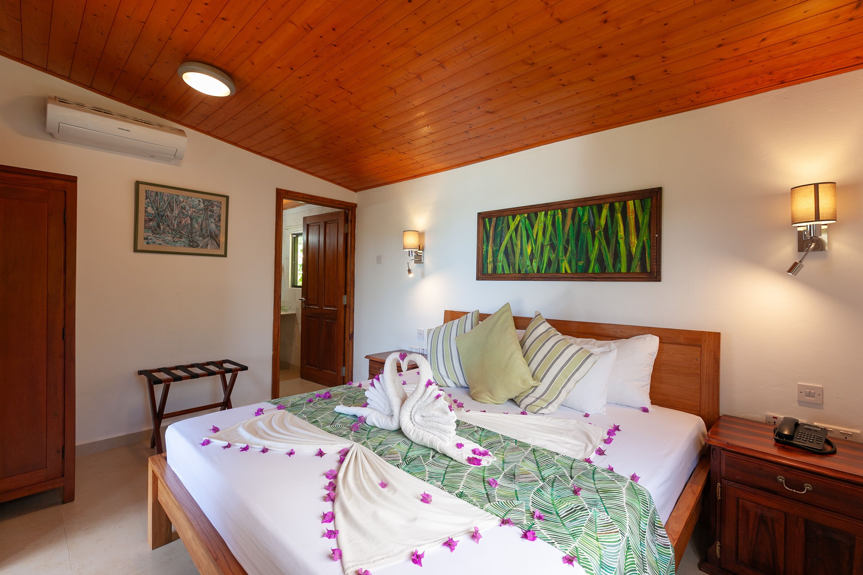 Habitación de hotel con techo de madera, una cama con colcha estampada, dos lámparas fijadas a la pared y una mesita de noche con teléfono.