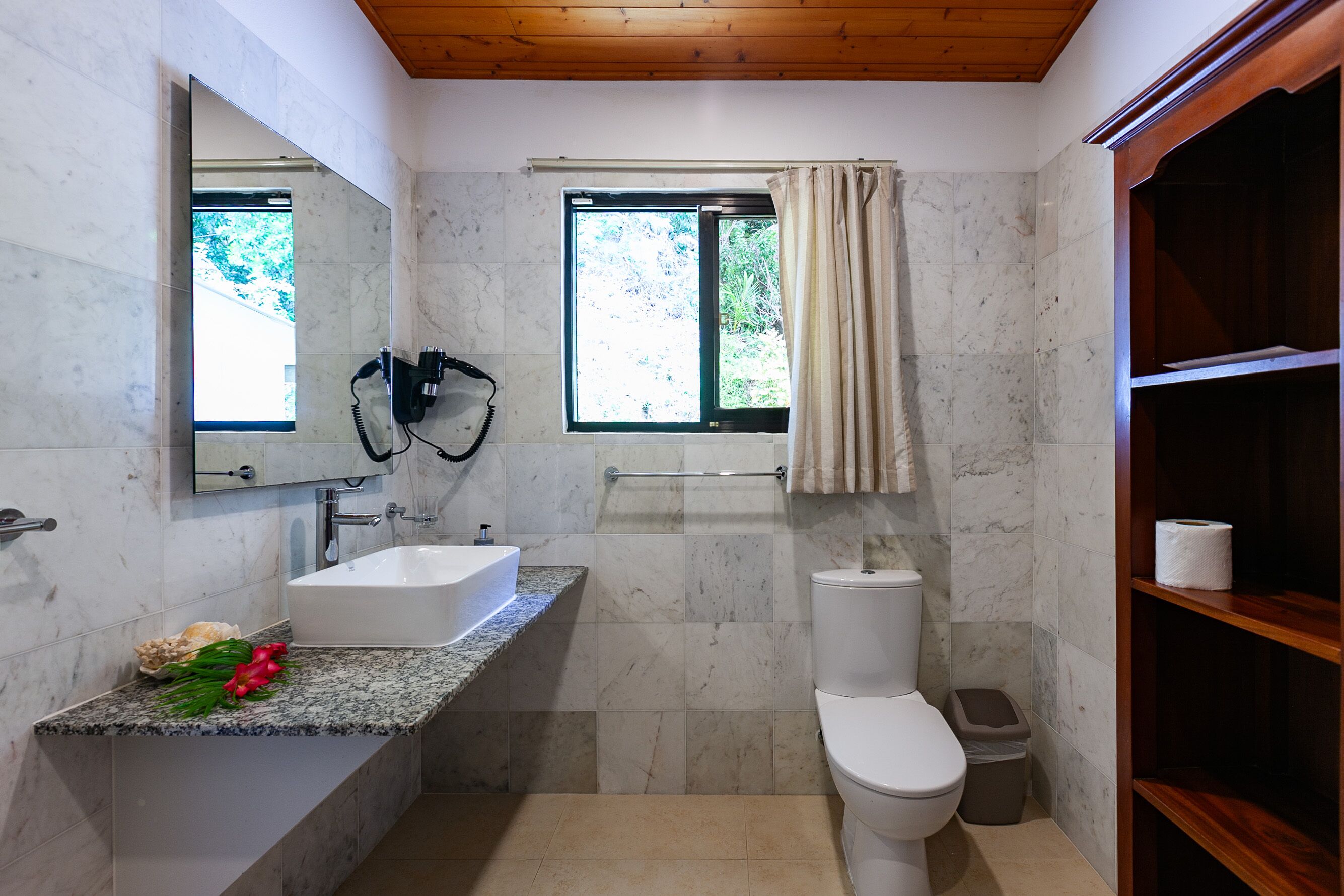 A bathroom with a marble sink, a toilet, a shower area, and a wooden shelf.