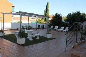 Ein Patio im Freien mit weißen Stühlen, einer Pergola und Kübelpflanzen.