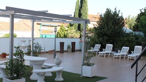 Een terras buiten met witte stoelen, een pergola en potplanten.