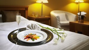 A neatly made bed with a tray of food, a glass of champagne, and a bouquet of flowers. - Dolce Villa Hotel (Prague)