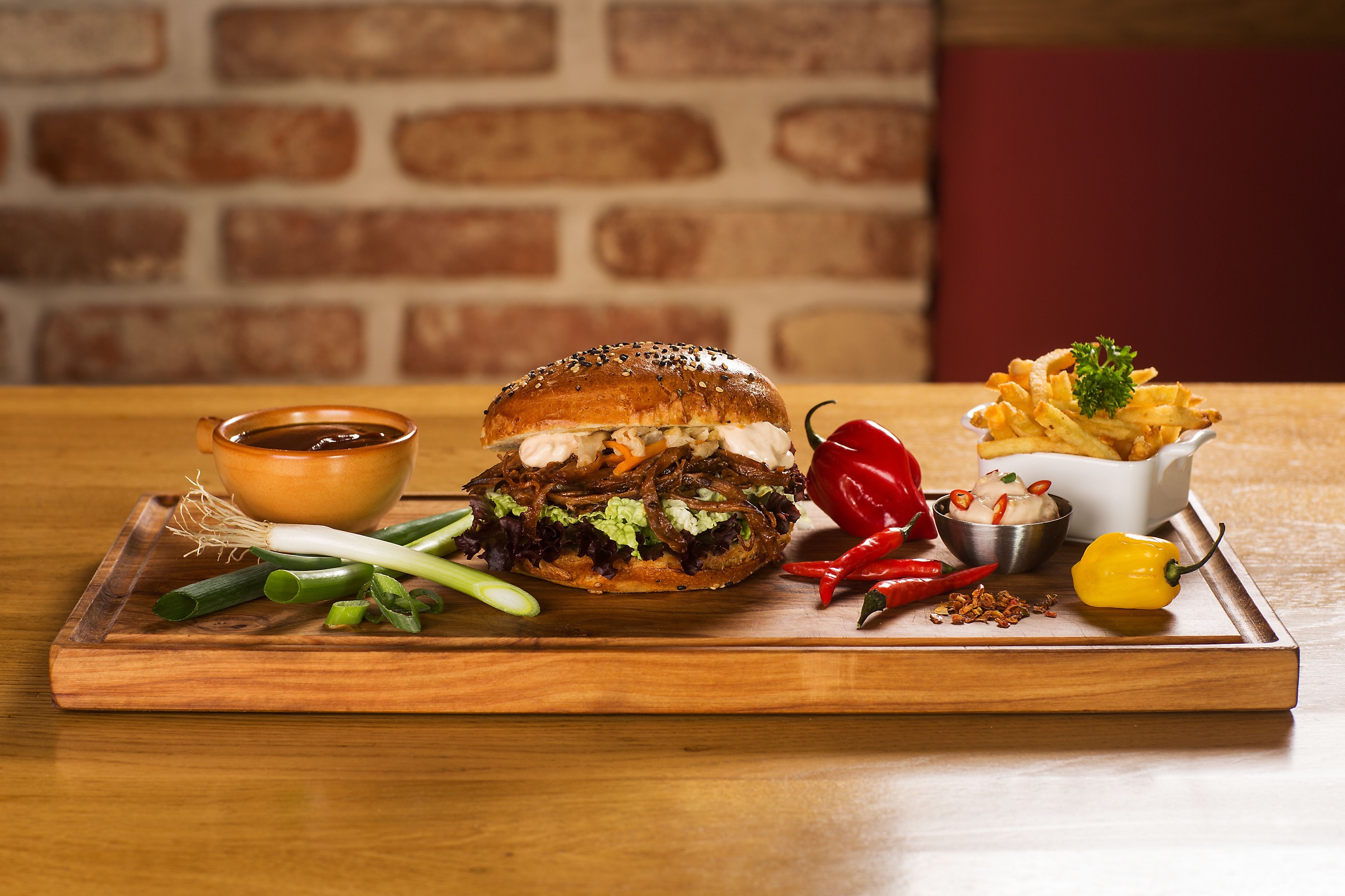 A burger with fries and condiments on a wooden board.