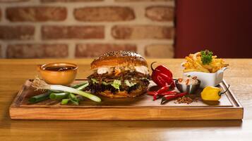 A burger with fries and condiments on a wooden board.