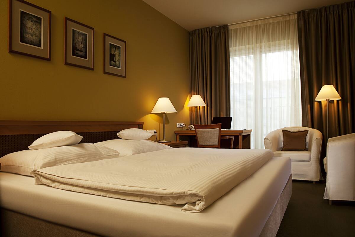 A hotel room with a large bed, two bedside tables, a desk, a chair, and a window with curtains.