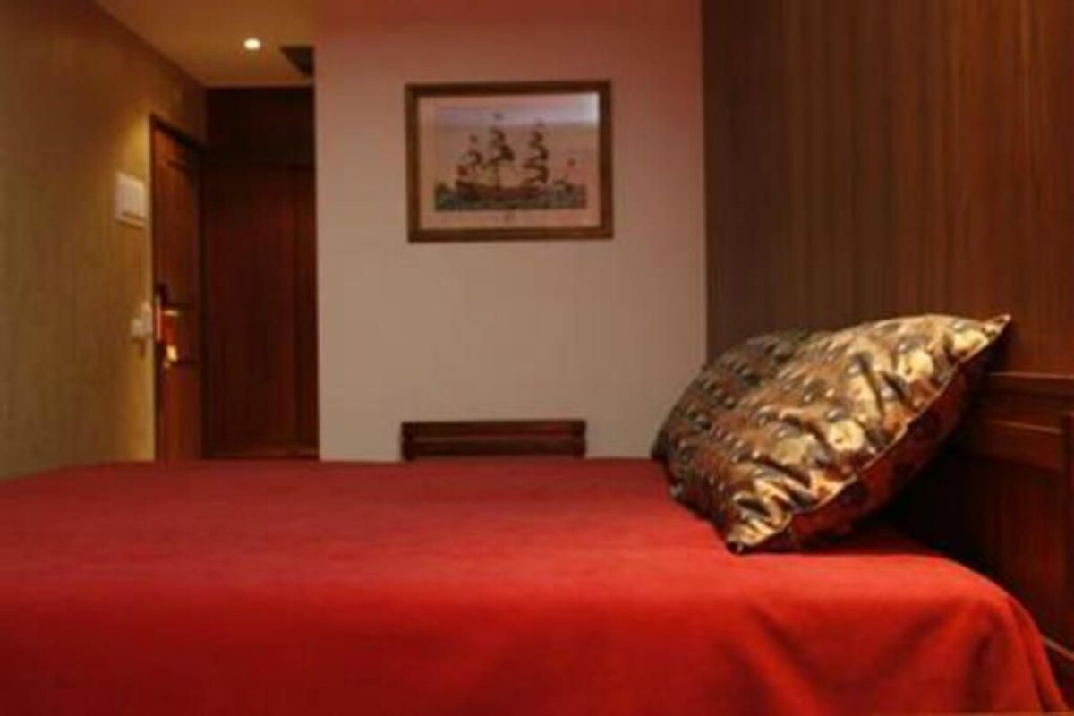 A hotel room with a bed, a wooden headboard, a framed picture on the wall, and a door.
