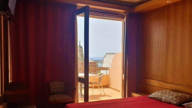 Une chambre d’hôtel avec un lit, une chaise, une petite table et un balcon donnant sur la ville.