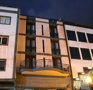 Un edificio de varios pisos con balcones y ventanas, que presenta un techo plano y una fachada de color claro.
