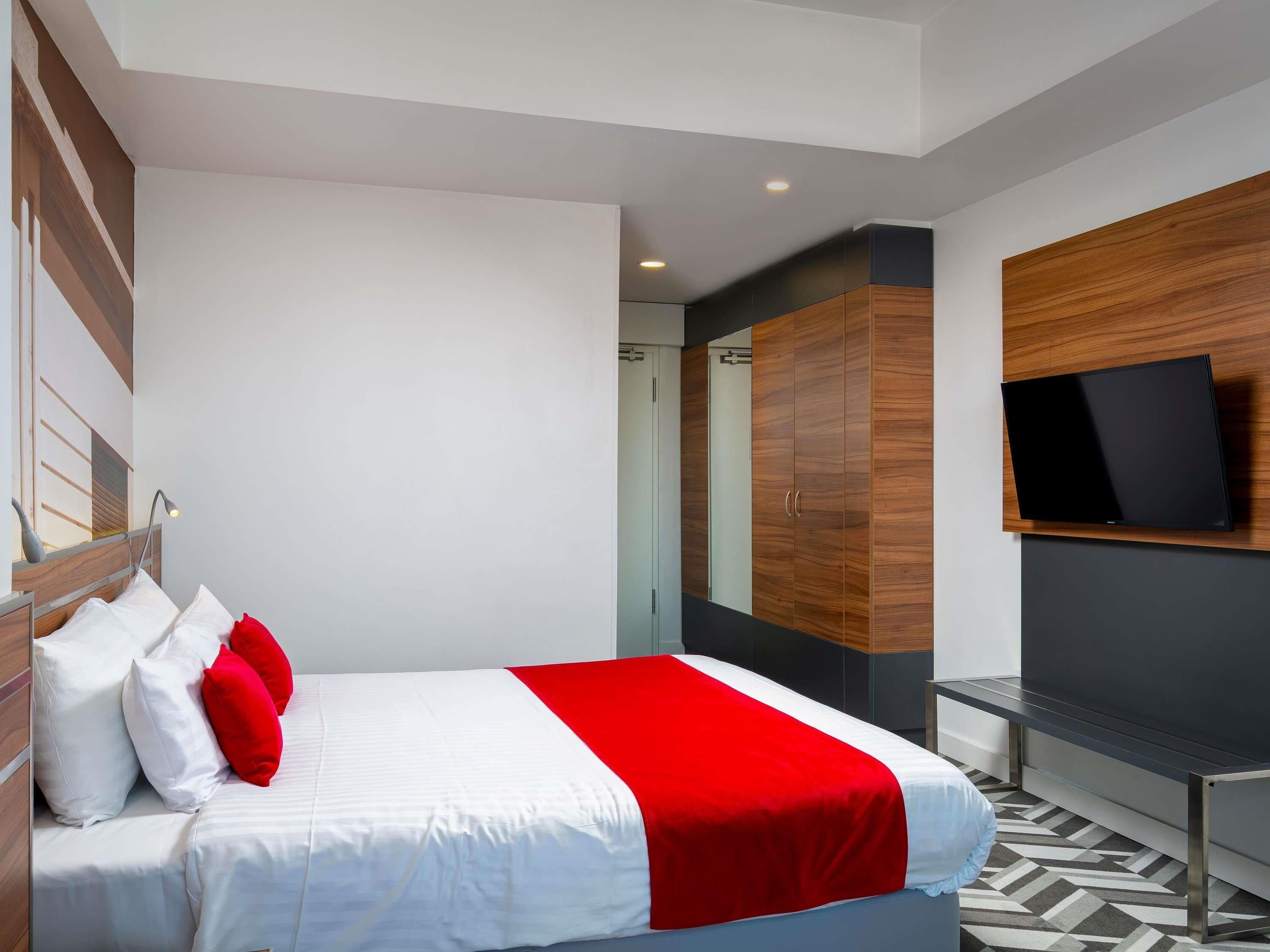 Una habitación de hotel moderna con cama, televisor montado en la pared y armario.