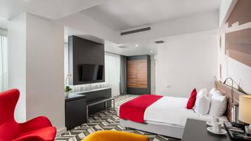 A modern hotel room with a bed, a desk, a TV, and a red chair.