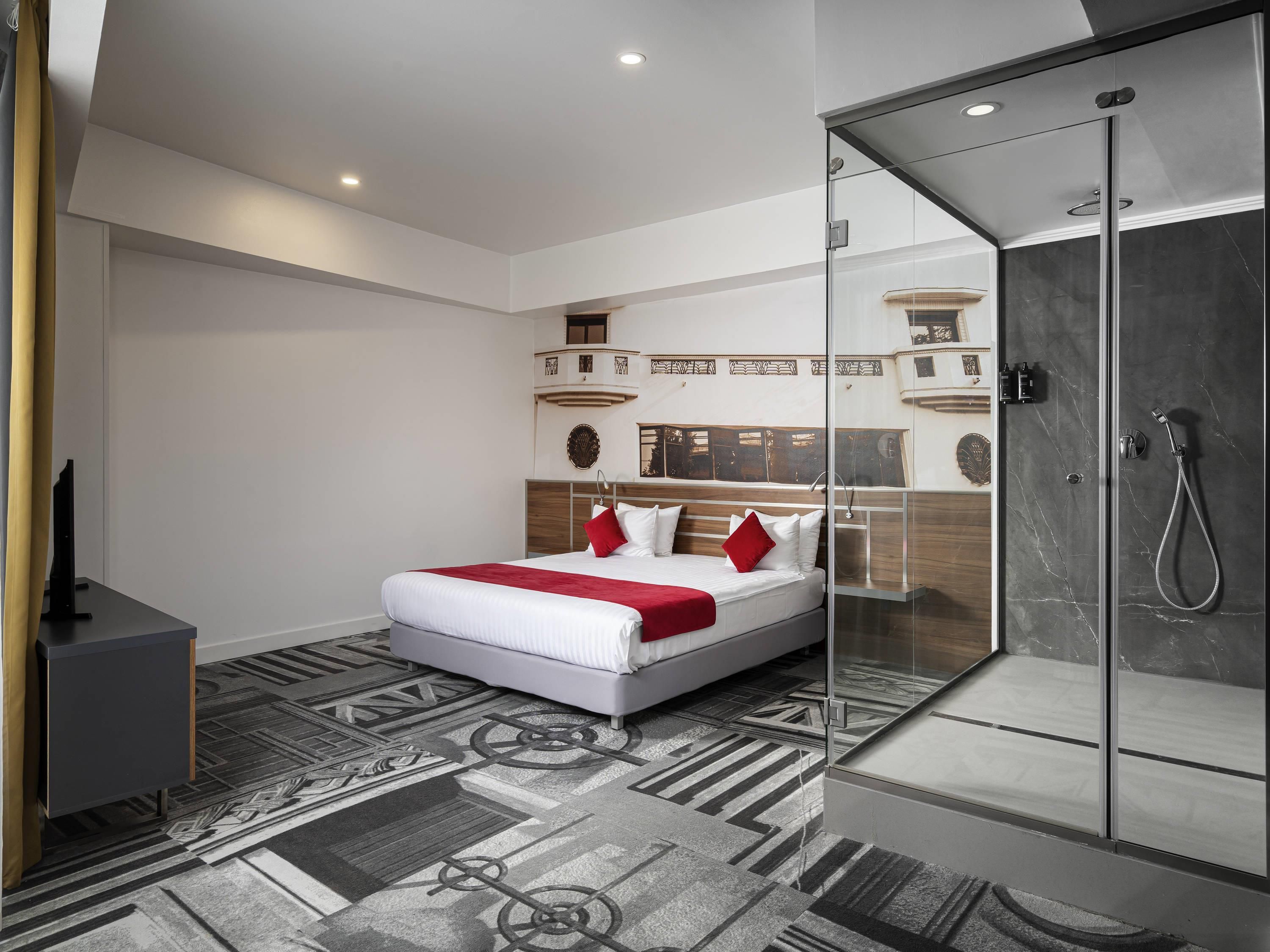 A modern hotel room with a bed, a glass-enclosed shower, and a patterned floor.