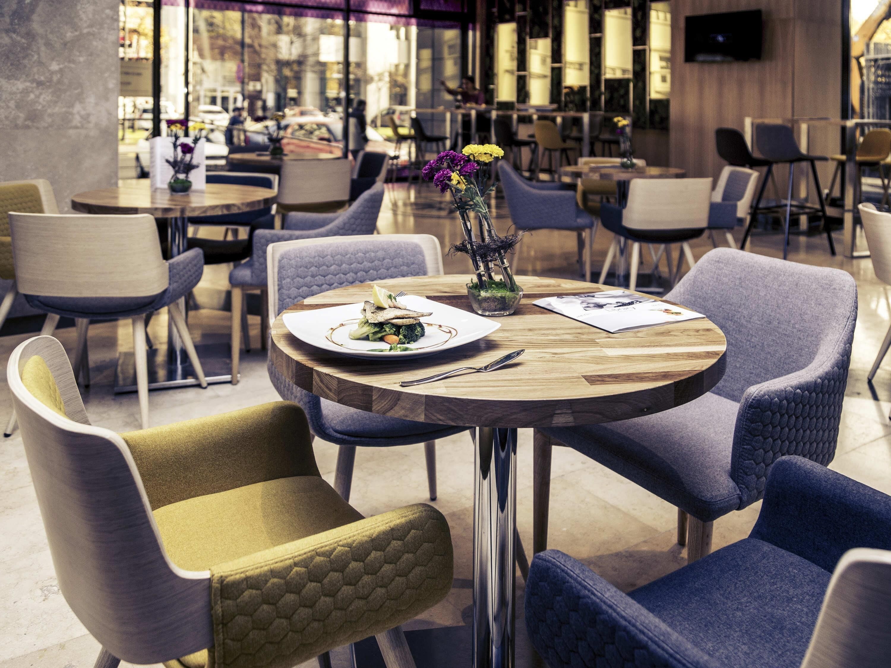En restauranginteriör med runda bord, bekväma stolar och en vas med blommor.