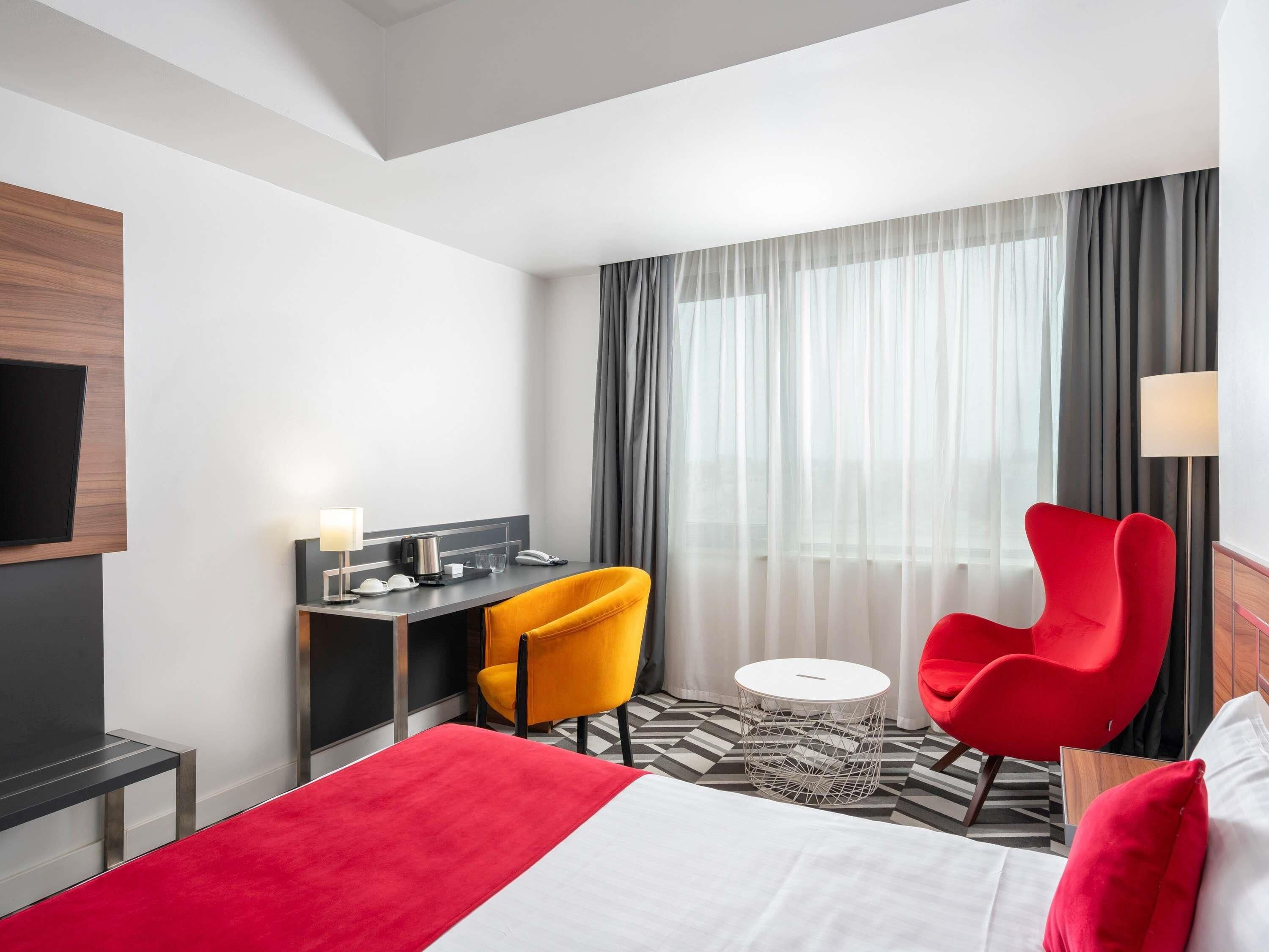 Een hotelkamer met een bed, een bureau, twee stoelen, een televisie en een raam met gordijnen.