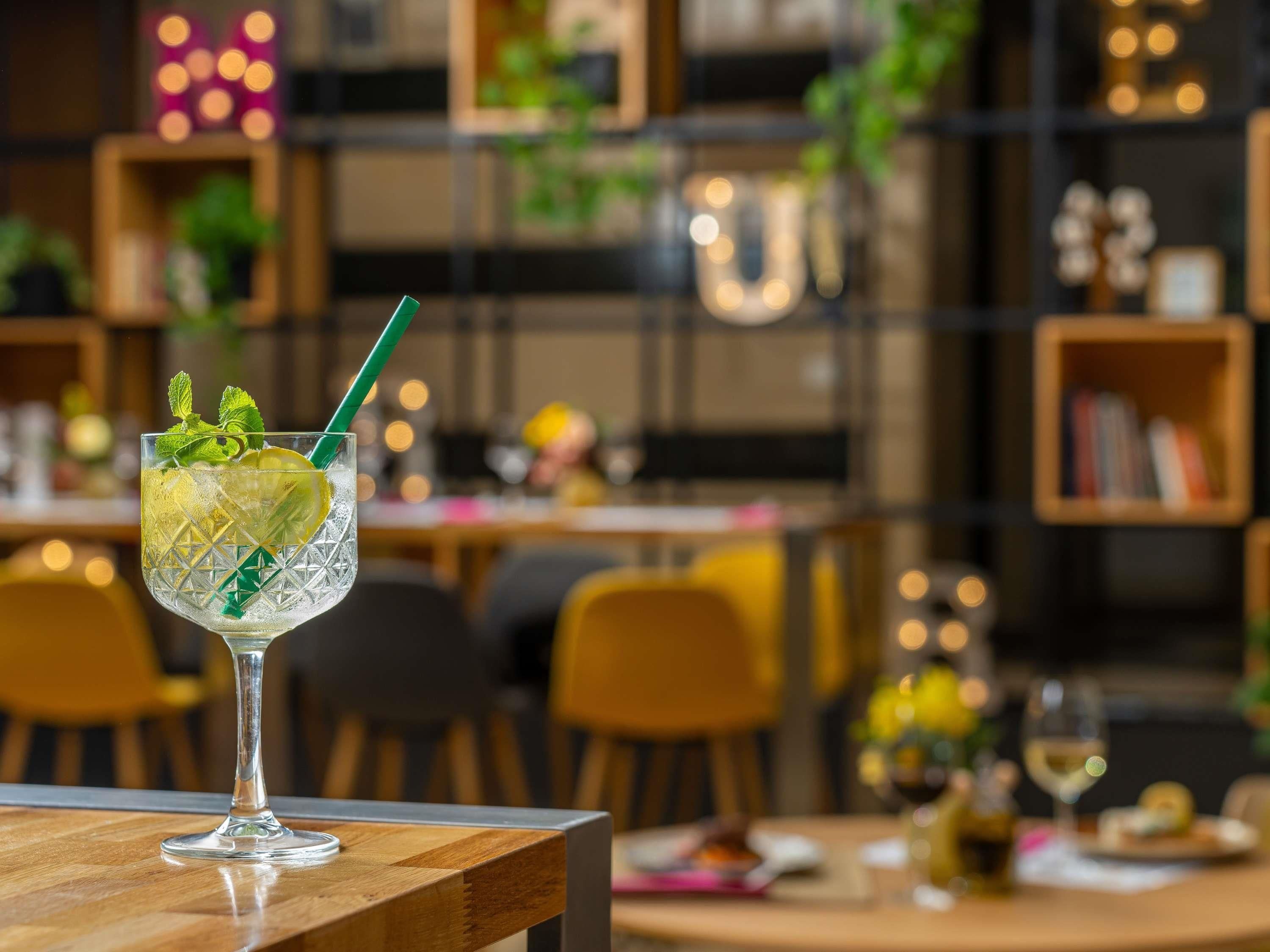 A cocktail glass with a straw on a wooden table in a restaurant setting.