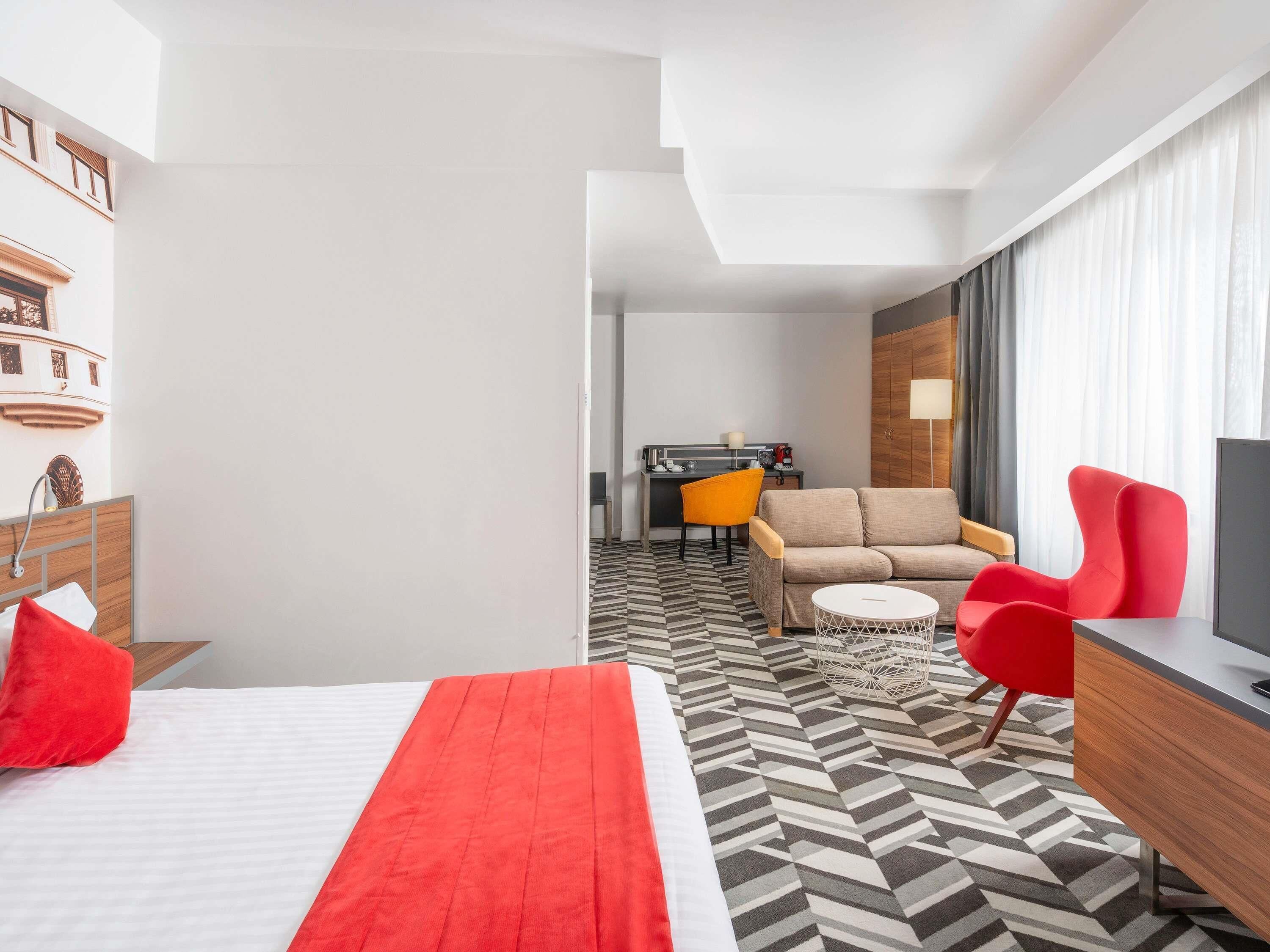 Hotellihuone, jossa on sänky, sohva, kirjoituspöytä, jossa on televisio, ja ruokailutila.