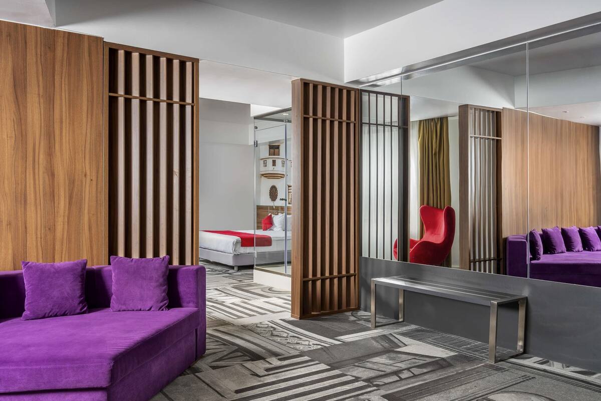 Une chambre d’hôtel moderne avec un canapé violet, un miroir et une moquette à motifs.