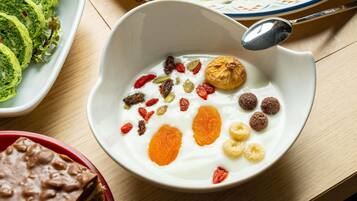 A bowl of yogurt with various toppings, a plate of green rolls, and a dessert in a red dish.