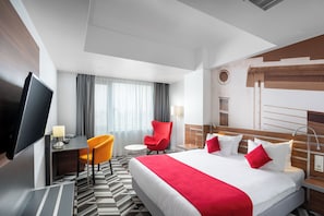 A hotel room with a large bed, a desk with a chair, a television, and a window with curtains. - Mercure Bucharest Unirii (Bucharest)