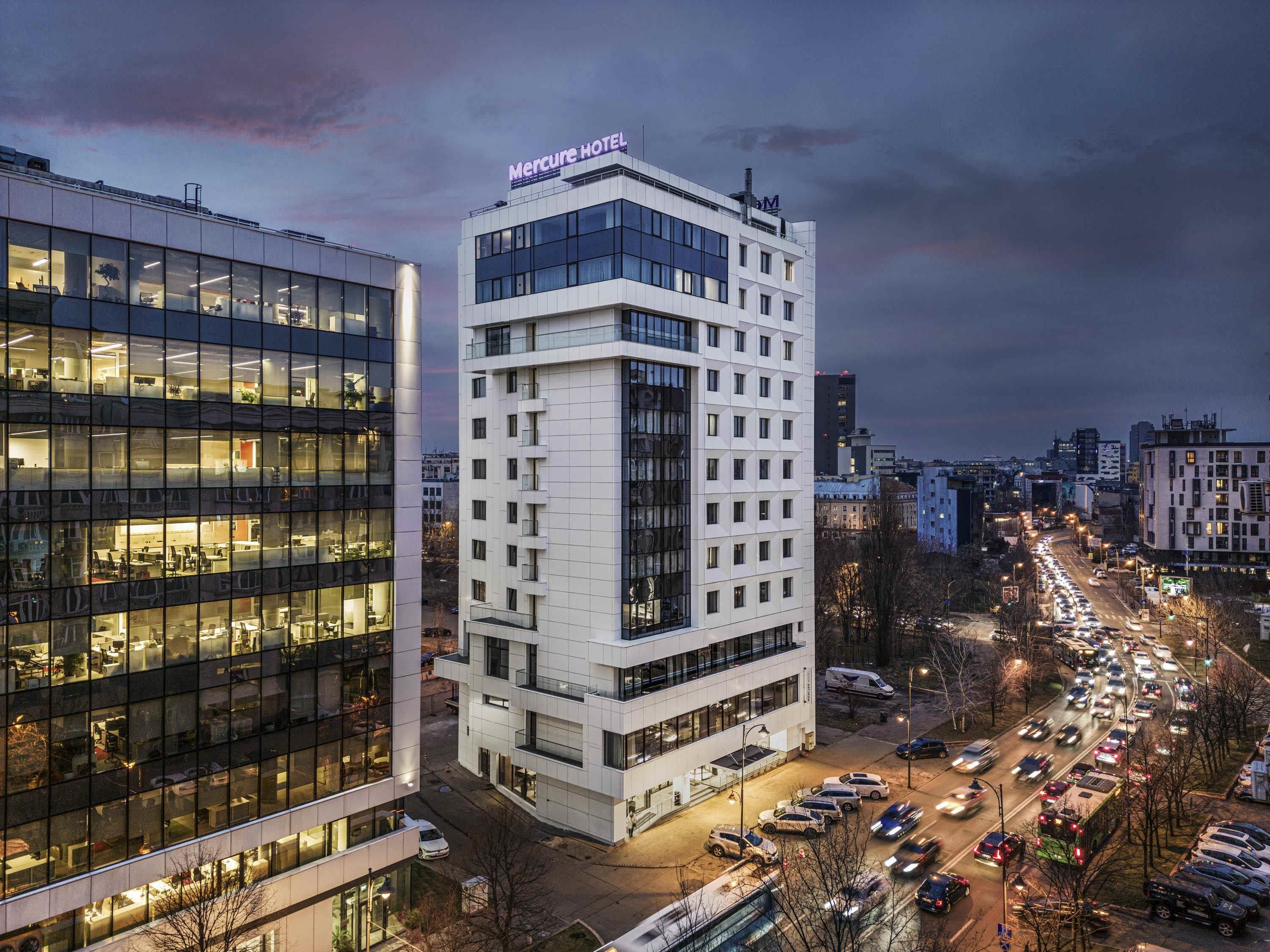 Un hôtel moderne, avec une enseigne bien visible, plusieurs étages et un parking où sont garées des voitures.