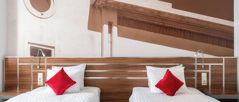 Habitación de hotel con dos camas, cada una con un almohadón rojo, cabecero de madera y diseño moderno.