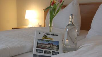 Ein ordentlich bezogenes Bett mit einer Broschüre mit dem Titel 'Information' und einer Wasserflasche darauf.
