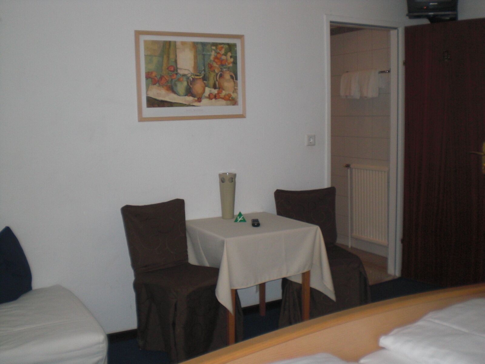 A small room with a bed, a table with a vase, two chairs, and a painting on the wall.