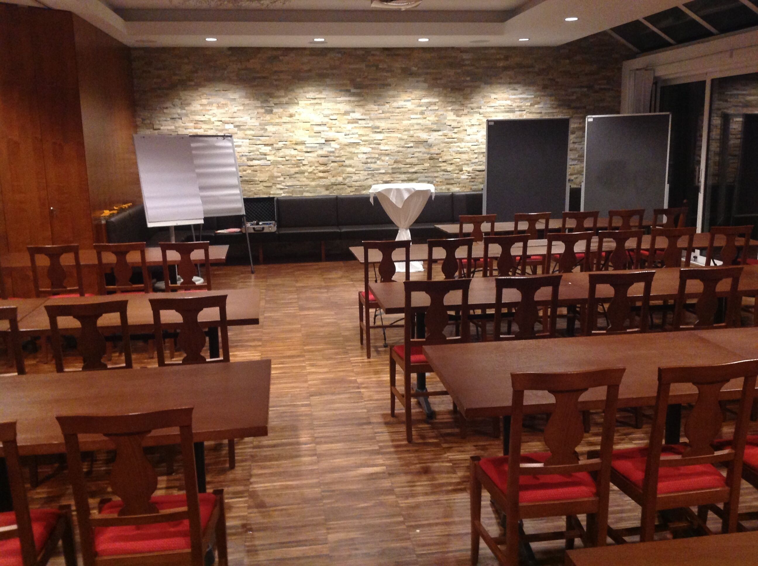 Ein Konferenzraum mit Holztischen und -stühlen, einer Steinwand und einer Whiteboard-Tafel.