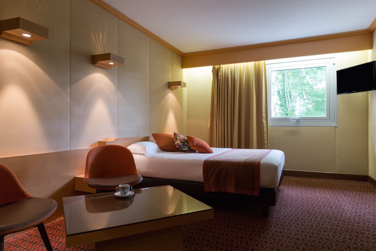 Ein Hotelzimmer mit Bett, Schreibtisch, Stuhl, Fernseher und einem Fenster mit Vorhängen.