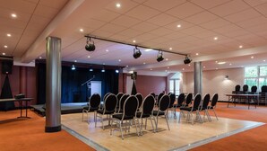 Un salón de conferencias con un escenario, sillas dispuestas en filas, un atril y una pared de ladrillo.