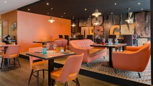 Un restaurante moderno con decoración naranja y negra, que presenta asientos acolchados e iluminación colgante.