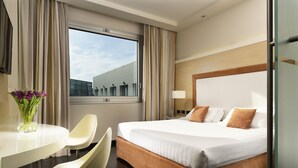 Ein Hotelzimmer mit Bett, Schreibtisch, Stuhl und Fenster mit Blick auf ein Gebäude.