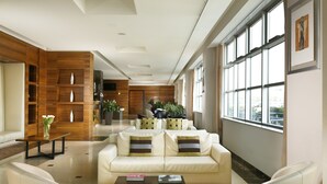 Ein modernes Wohnzimmer mit einer Couch, einem Couchtisch und Büchern. Ein Bücherregal aus Holz und ein großes Fenster mit Ausblick sind ebenfalls vorhanden.
