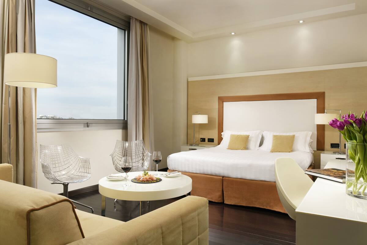 Habitación de hotel con una cama grande, una mesa de comedor redonda, un sofá y vistas a la ciudad.