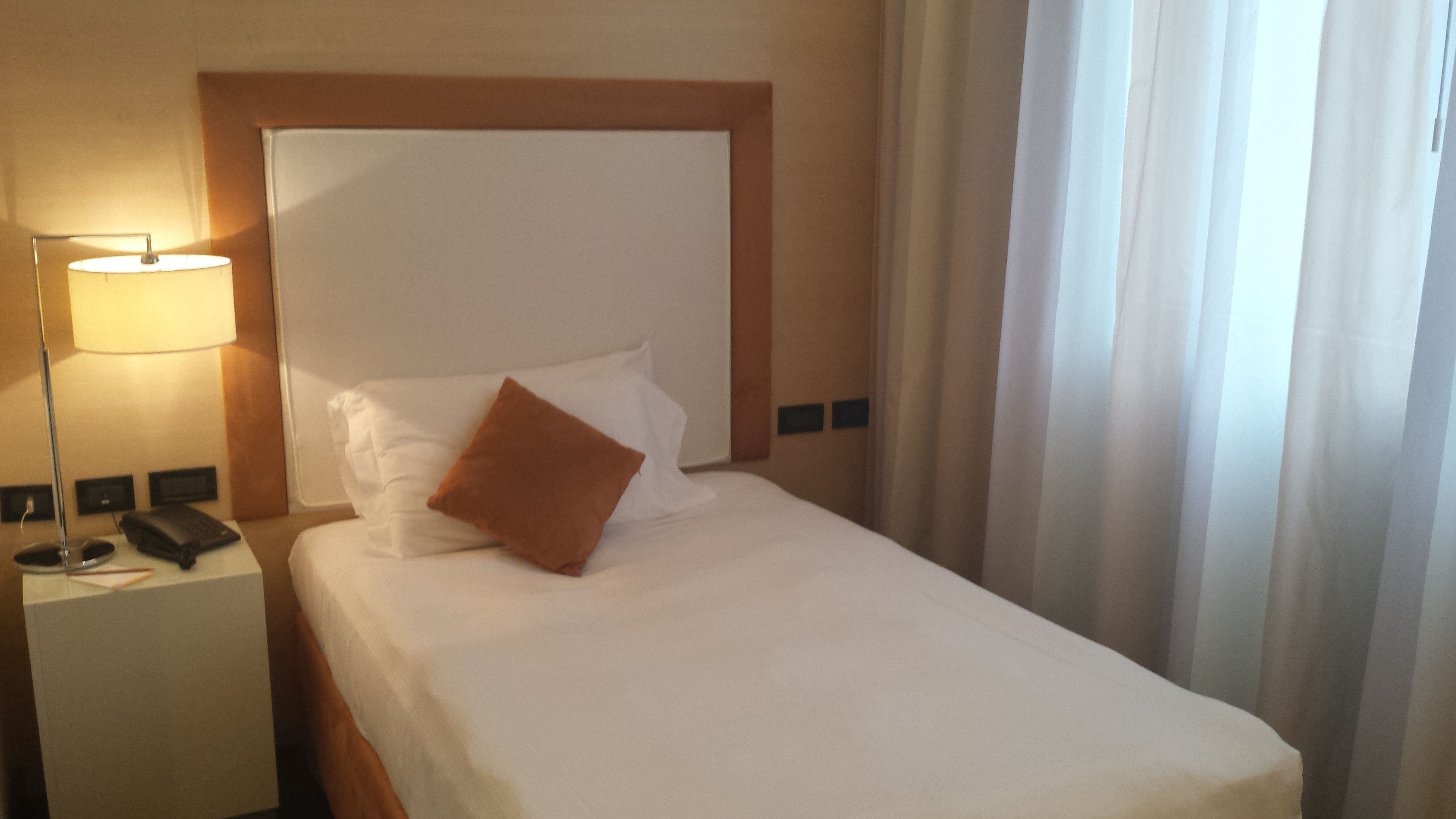 A hotel room with a neatly made bed, a bedside lamp, a telephone, and a nightstand.