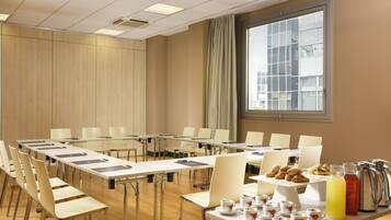 Un salón de conferencias con una larga mesa, sillas y una mesa de buffet con pasteles y bebidas.