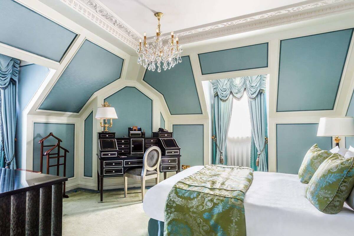 A room with a large bed, a desk, and a chandelier.