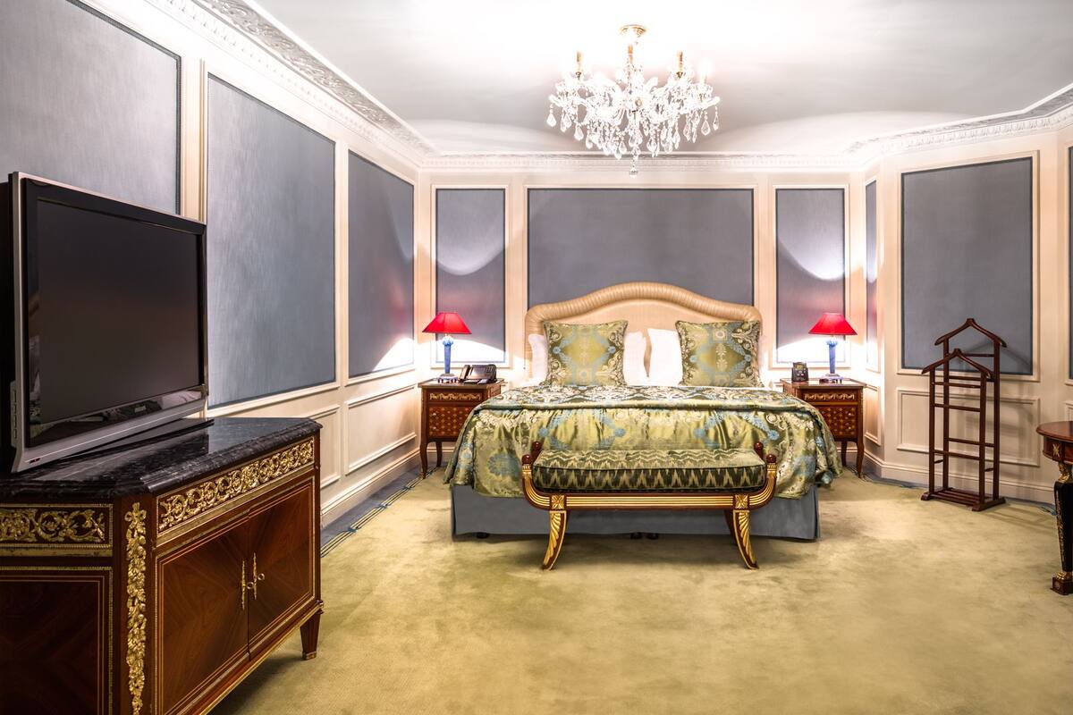 A luxurious bedroom with a large bed, ornate furniture, and a chandelier.