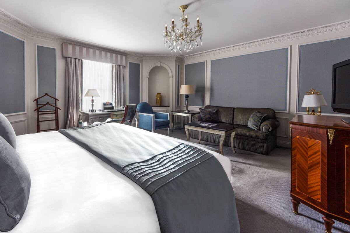 A hotel room with a large bed, a sofa, a chair, a desk, and a television.