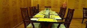 A dining room with a long table set for a meal, surrounded by wooden chairs. - Saj Luciya (Thiruvananthapuram)