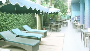 A covered outdoor seating area with lounge chairs and tables, surrounded by greenery. - Saj Luciya (Thiruvananthapuram)
