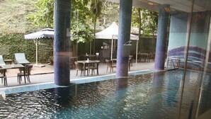 An indoor swimming pool with tiled walls and pillars, surrounded by lounge chairs and tables. - Saj Luciya (Thiruvananthapuram)